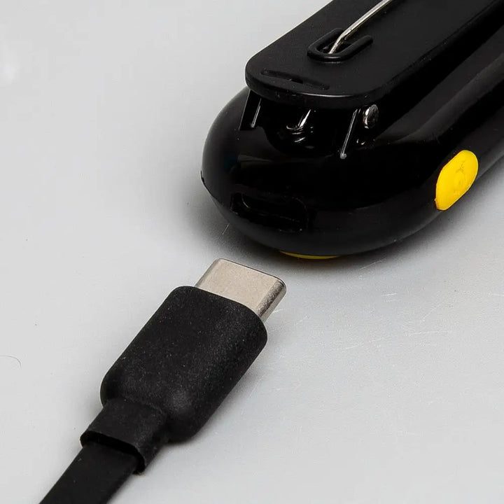 Black electronic device with a yellow button and USB-C cable on a light gray background