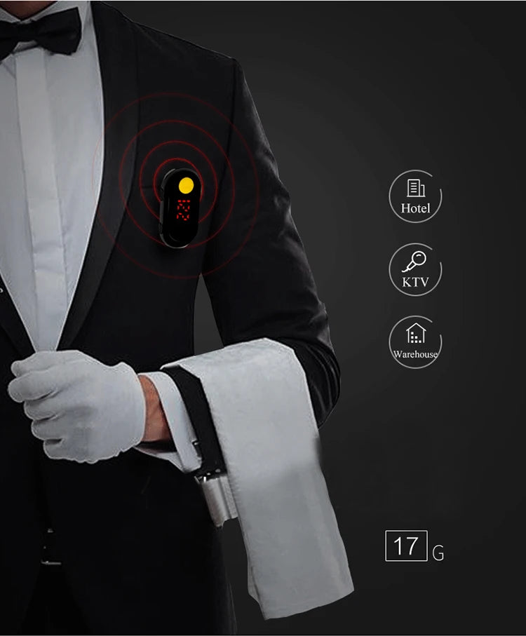 Person wearing a tuxedo with a device on their sleeve, set against a dark background.