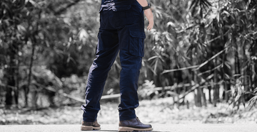 Person wearing dark blue pants and shoes standing outdoors with a natural background