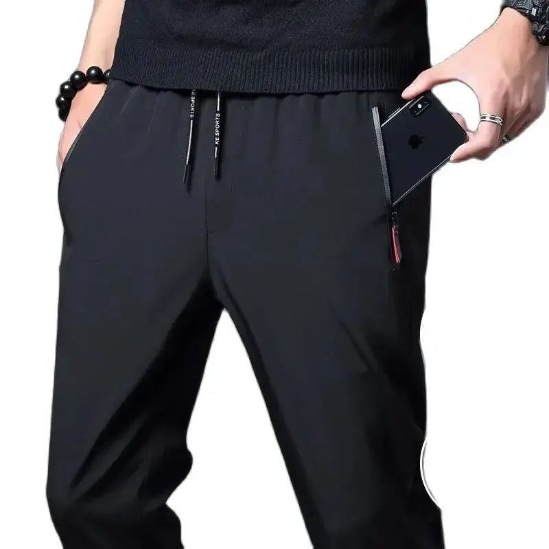 Person wearing black pants holding a phone on a white background
