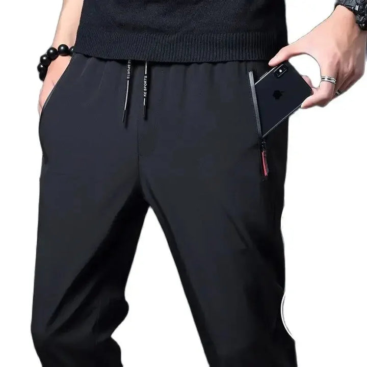 Person wearing black pants holding a phone on a white background
