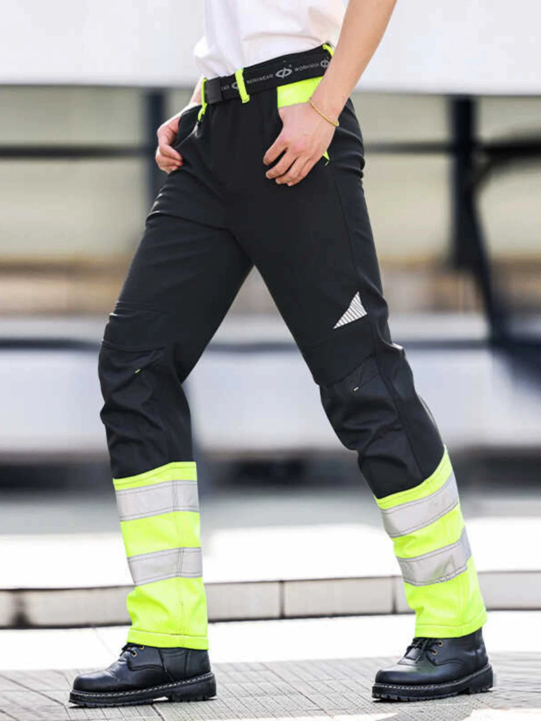 Person wearing high-visibility work pants with reflective stripes on a blurred background