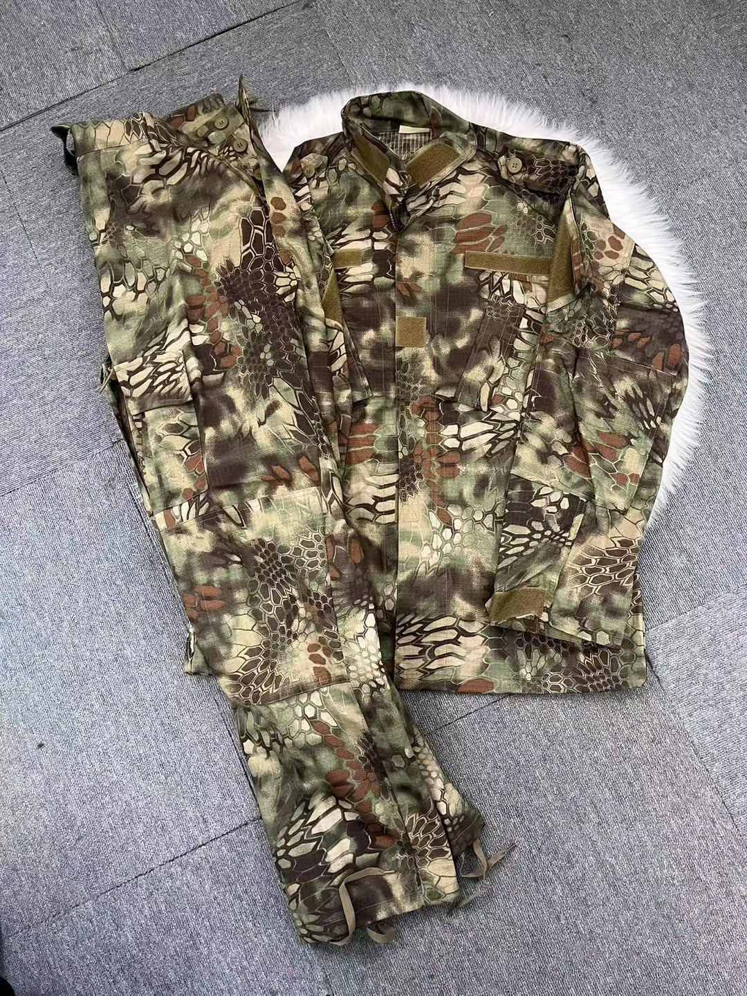 Camouflage military uniform with jacket and pants on a gray floor.