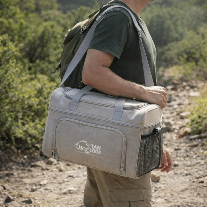 Person carrying a gray cooler bag with 'Stan' branding in a natural setting.