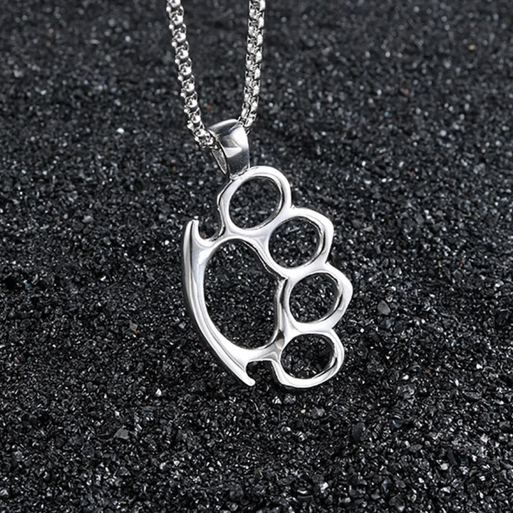 Silver knuckle duster pendant on a chain against a black sand background