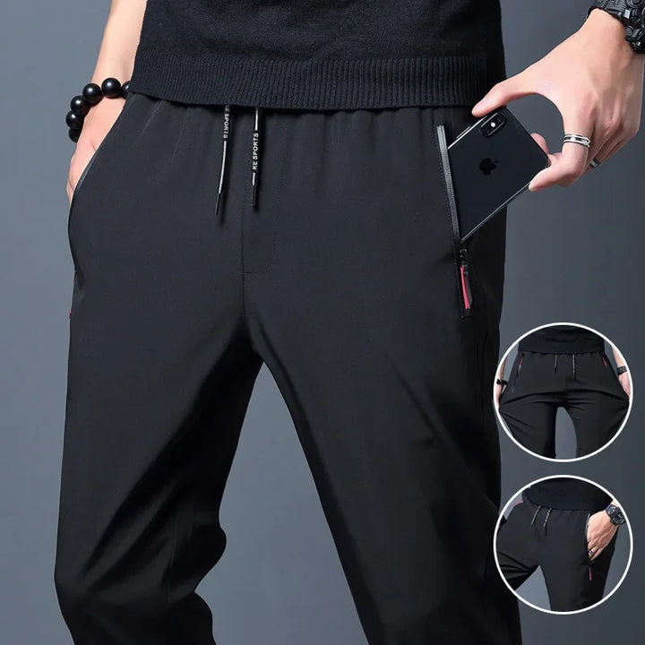 Person wearing black pants with a phone in the pocket on a gray background