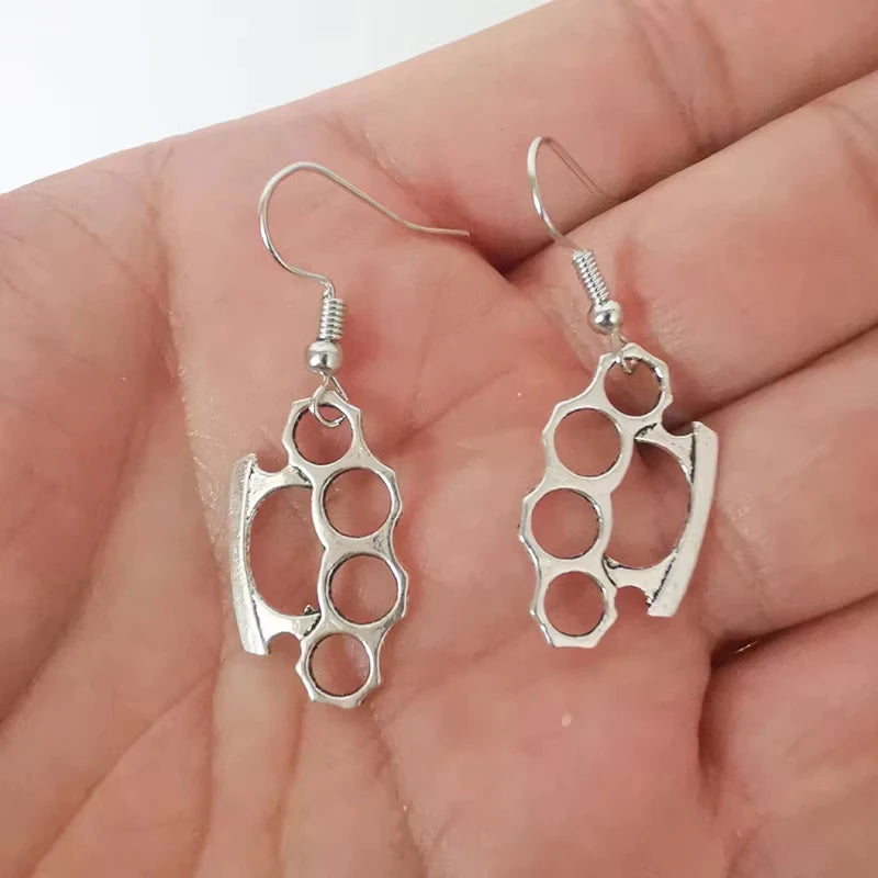Silver knuckle duster earrings held in a hand against a neutral background