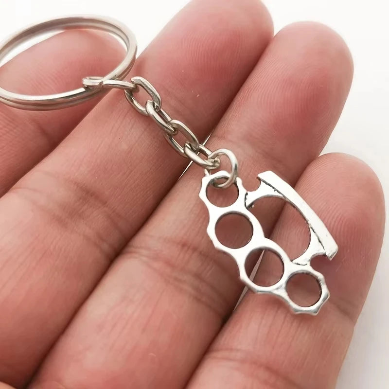 Silver knuckle duster keychain held in a hand against a white background