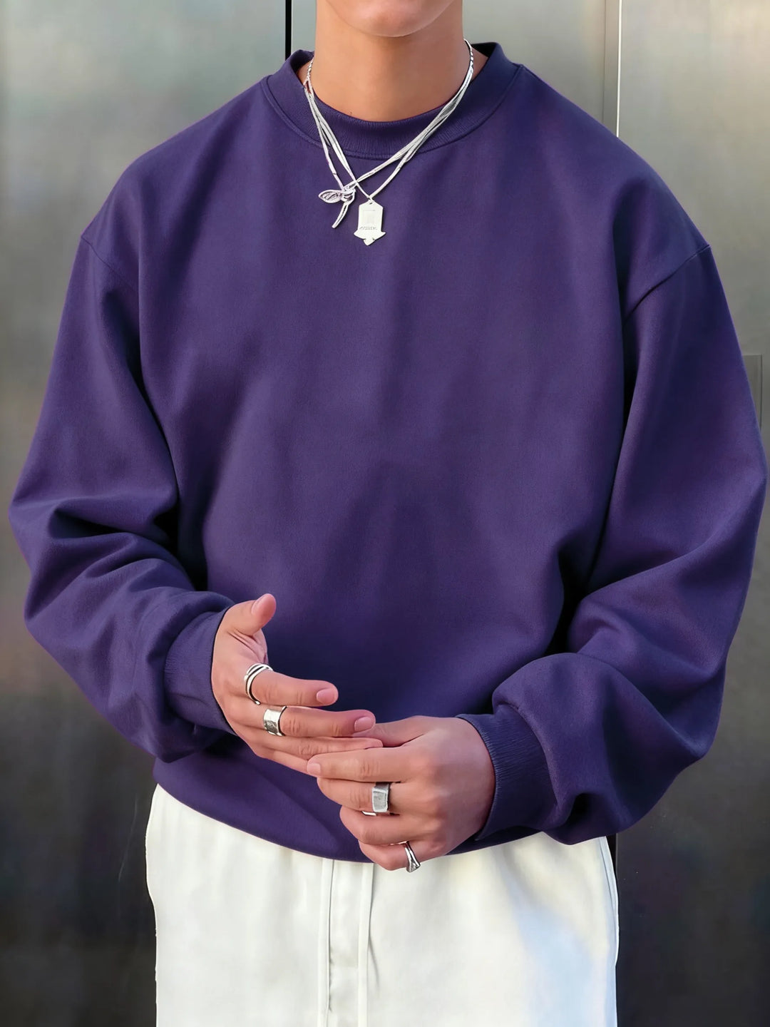 Person wearing a purple sweatshirt and white pants with a neutral background