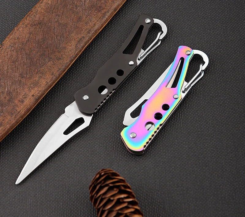 Two pocket knives, one black and one with a rainbow finish, on a dark surface.