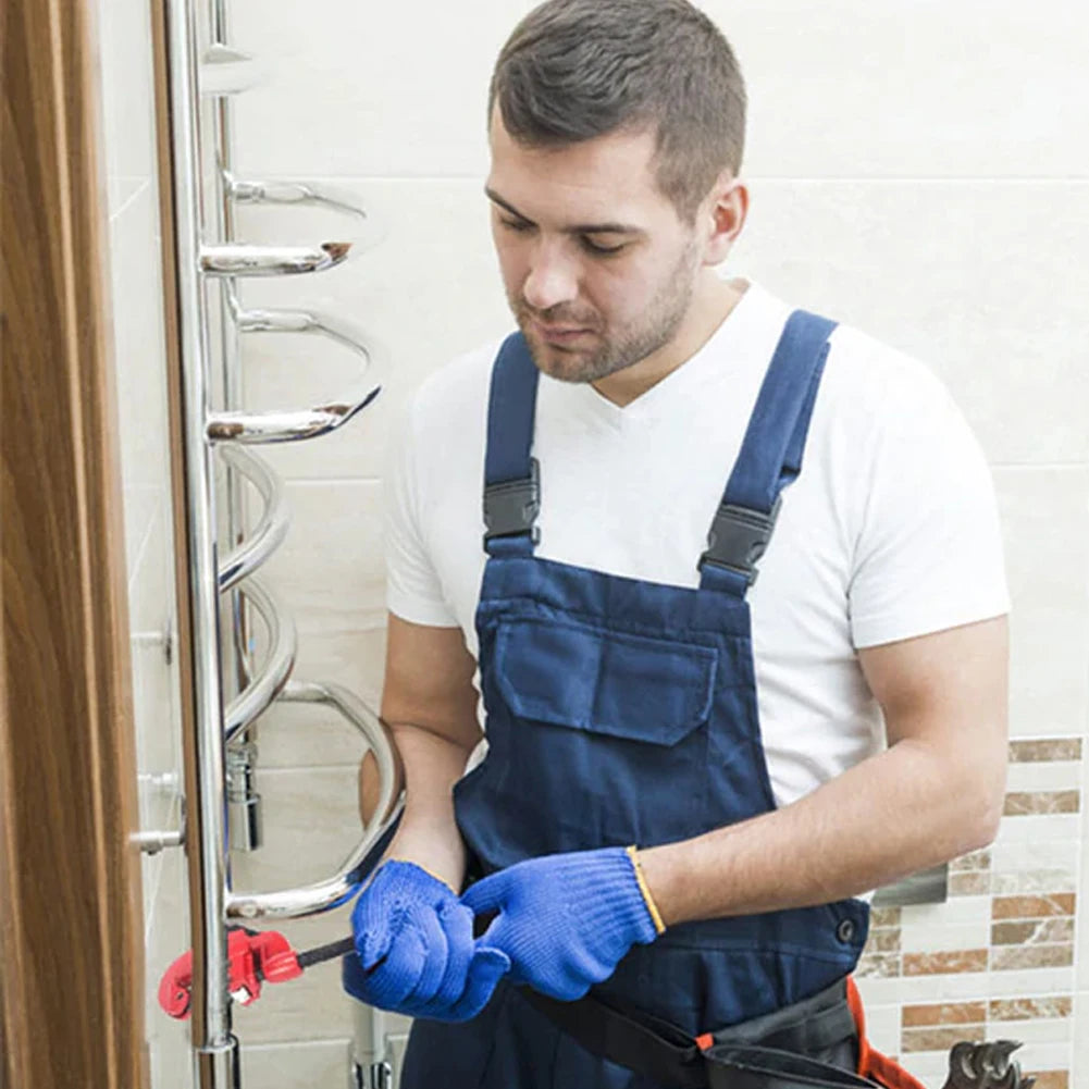 Man in blue overalls and gloves cutting  a pipe in a bathroom.