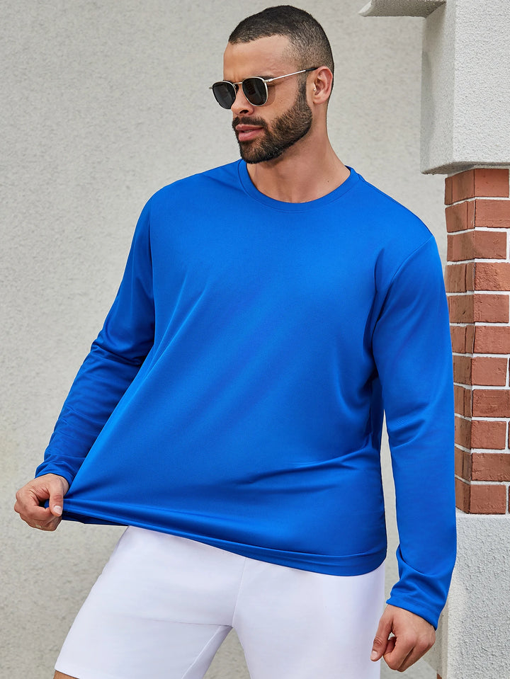 Man wearing a blue long-sleeve shirt and white shorts standing against a light gray wall.