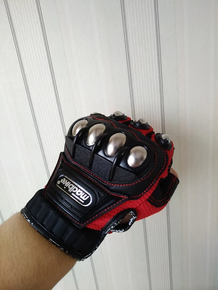 Black and red glove with metallic accents held against a white wooden panel background