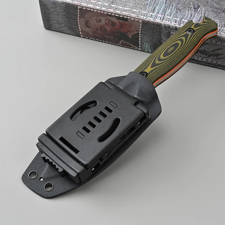 Black sheath with a knife featuring a green and orange handle on a gray surface.