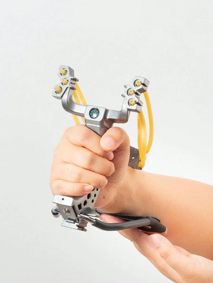 Hand holding a metal slingshot against a light gray background