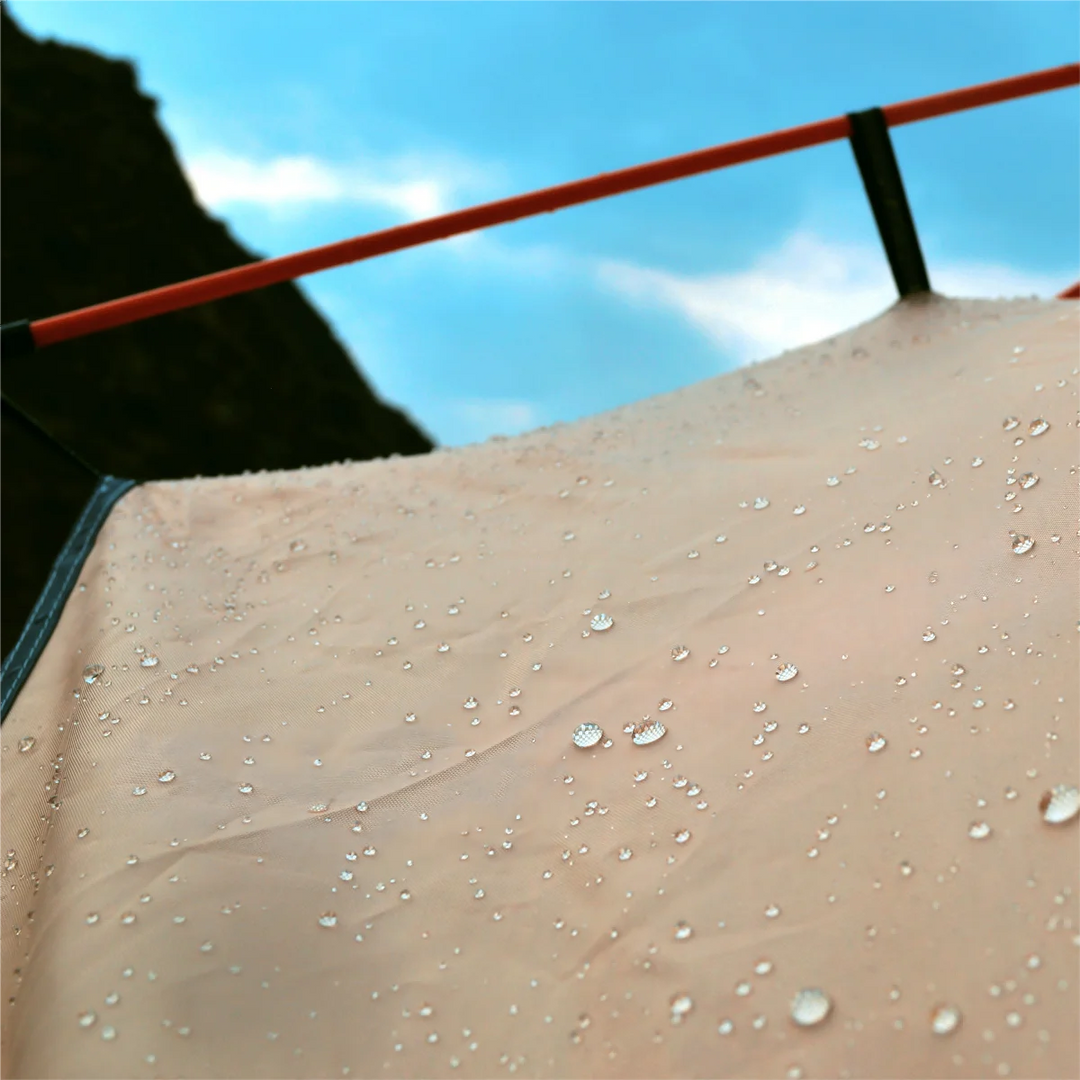 Close-up of a tent with water droplets on its surface against a blue sky.