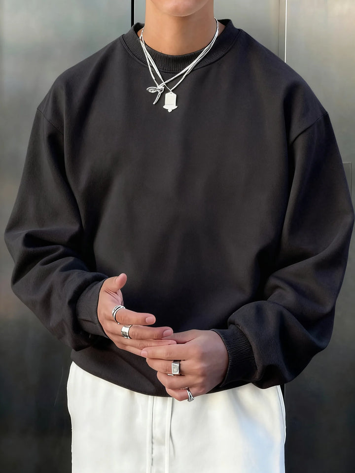 Person wearing a black sweatshirt and white pants with a neutral background