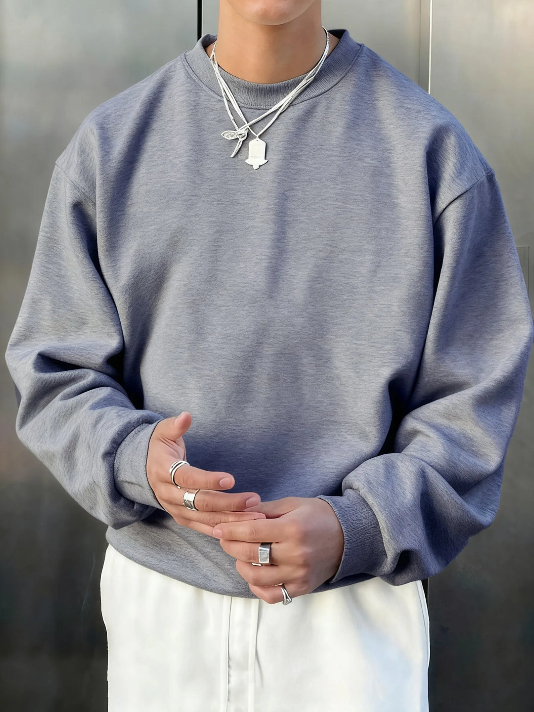 Person wearing a gray sweatshirt and white pants with a neutral background
