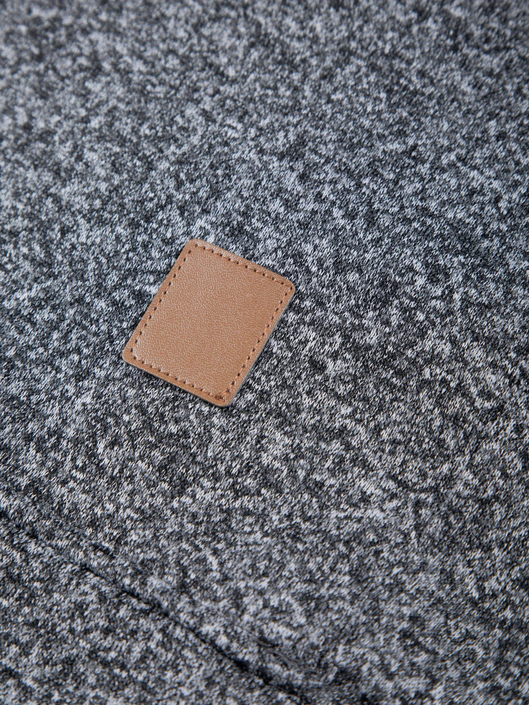 Close-up of a textured gray fabric surface with a brown leather patch.