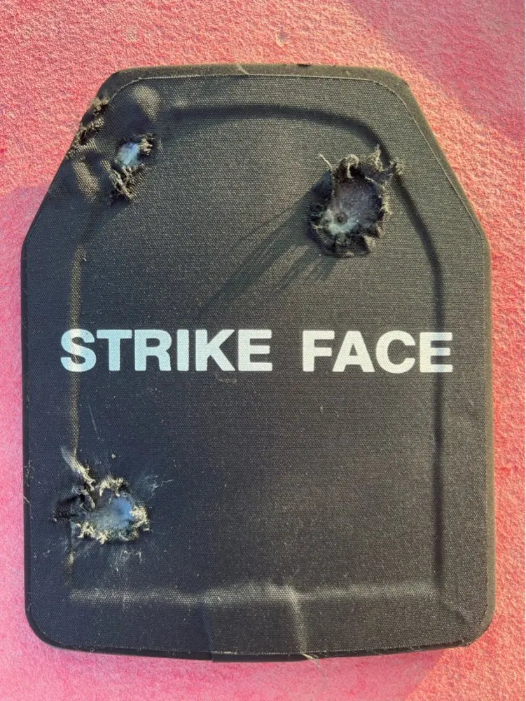 Black protective plate labeled 'Strike Face' with bullet holes on a pink background