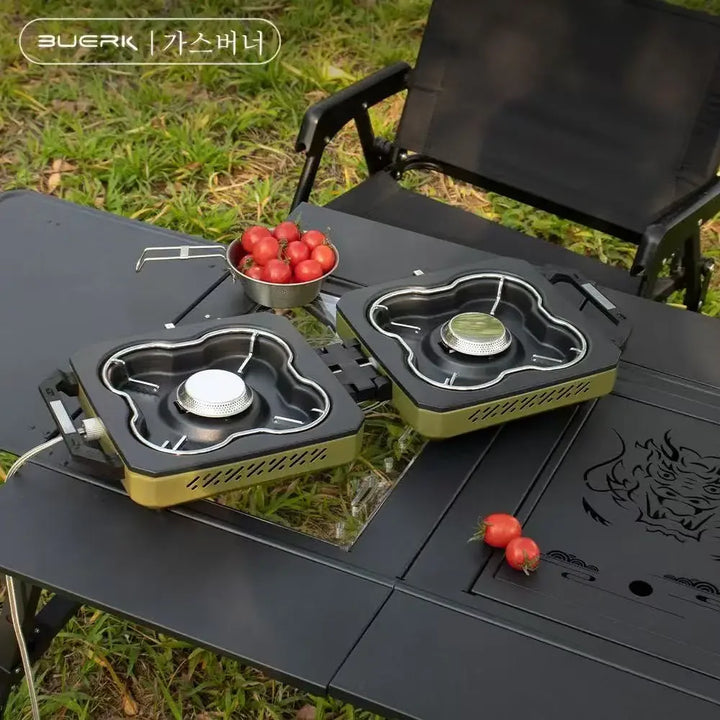 Portable camping stove with two burners on a black table outdoors.