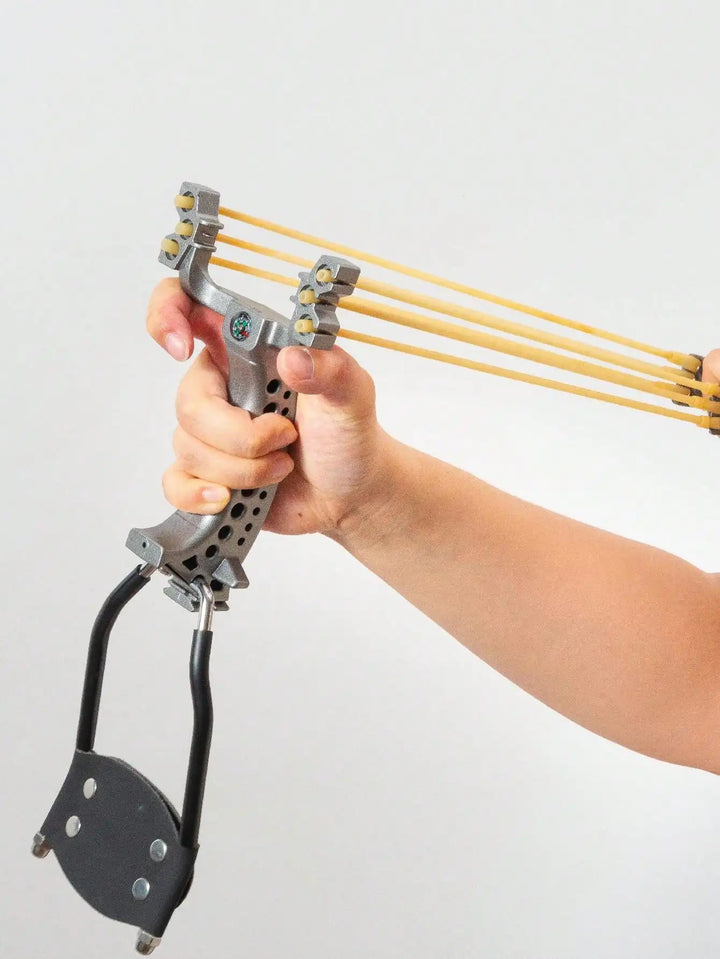 Hand holding a mechanical slingshot with multiple yellow strings on a light gray background
