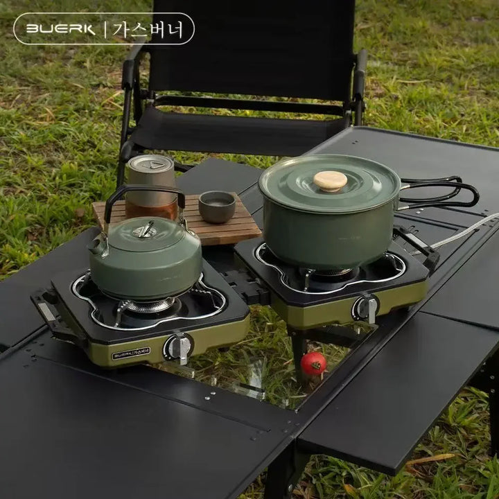 Two camping stoves with green pots on a table outdoors.