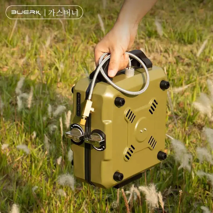 Hand holding a yellow gas burner in a grassy outdoor setting