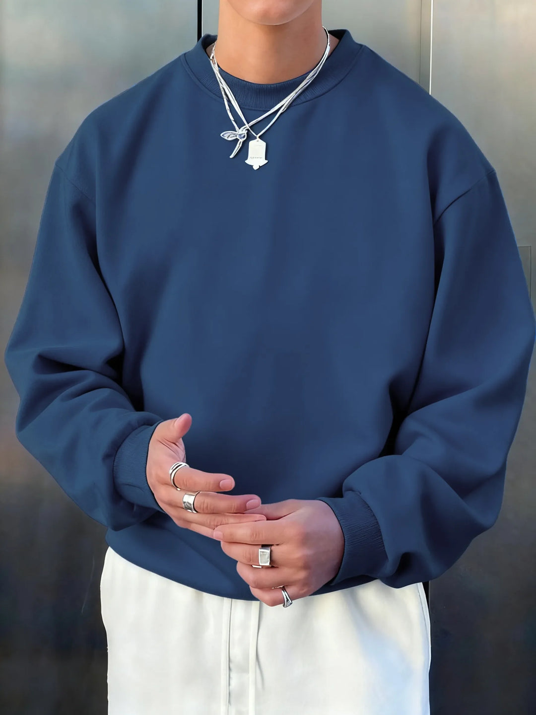 Person wearing a blue sweatshirt and white pants with a neutral background