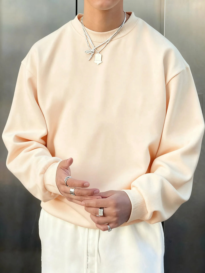 Person wearing a light pink sweatshirt and white pants with a neutral background