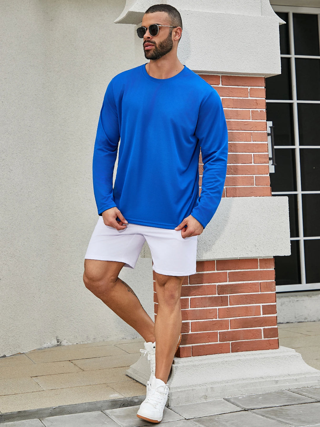 Man wearing a blue long-sleeve shirt and white shorts standing against a building.