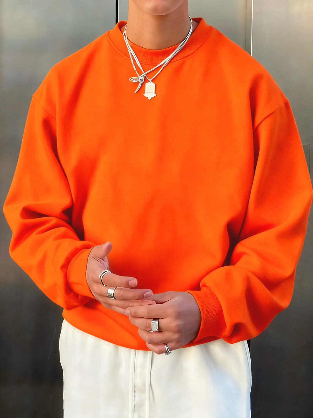 Person wearing an orange sweatshirt and white pants with a neutral background