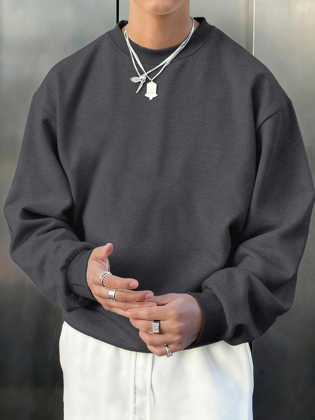 Person wearing a dark gray sweatshirt and white pants with a neutral background