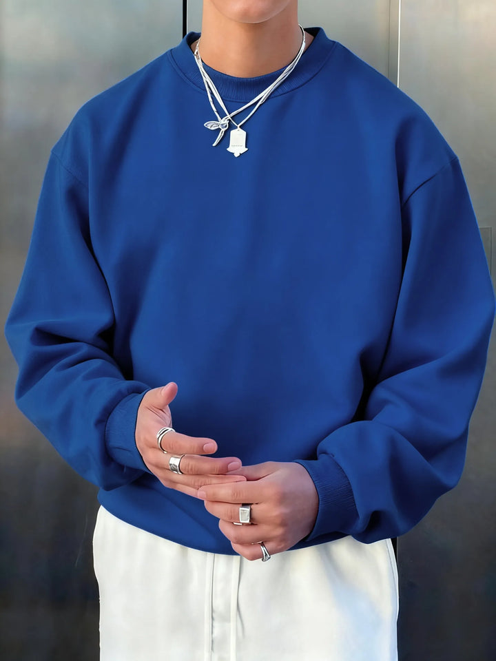 Person wearing a blue sweatshirt and white pants with a neutral background