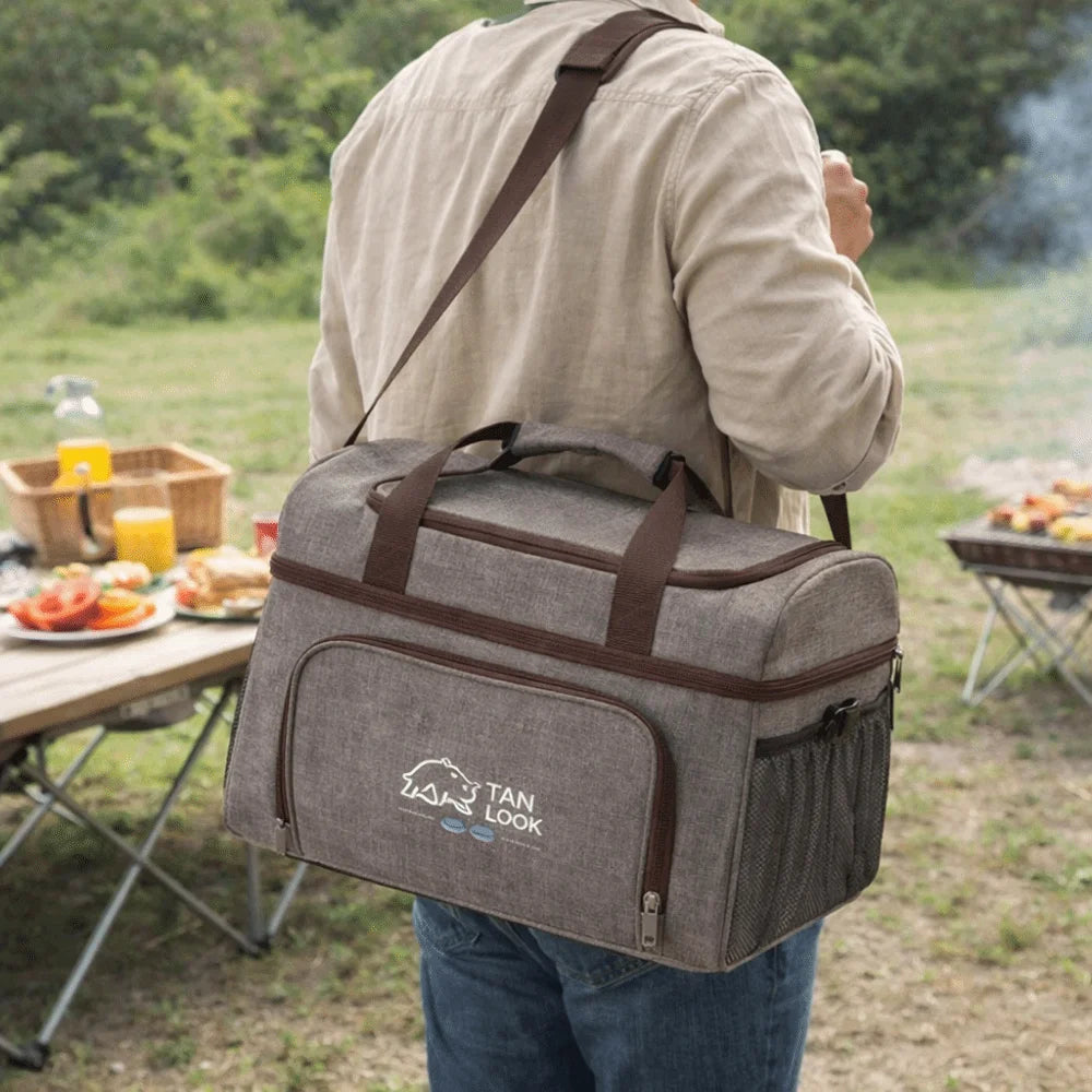 Person carrying a gray cooler bag with a shoulder strap in an outdoor setting.