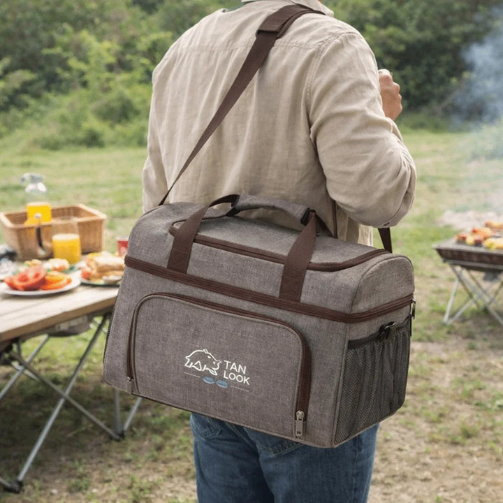 Person carrying a gray cooler bag with a shoulder strap in an outdoor setting.