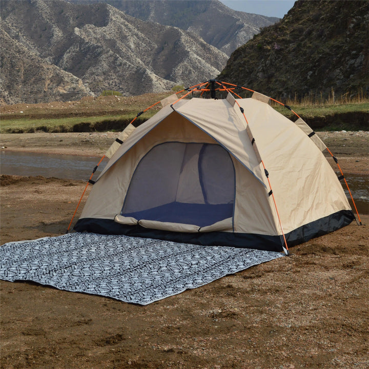 Beige camping tent with a blue groundsheet on a sandy beach with mountains in the background