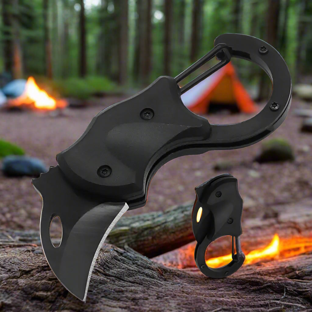 Compact folding knife with carabiner clip, shown at a forest campsite with a tent and fire in the background – perfect for outdoor survival, camping, or quick everyday utility.