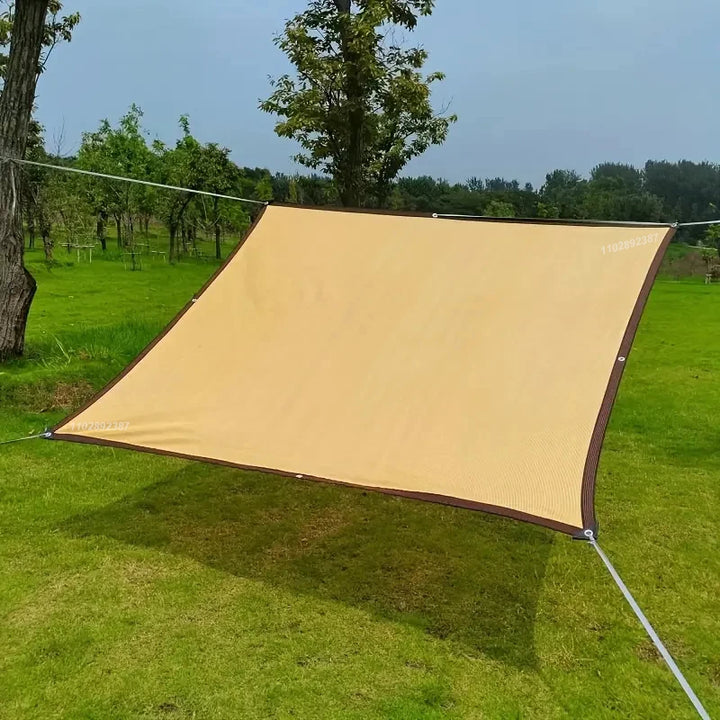 A beige rectangular shade sail installed in an open grassy yard using freestanding poles and ropes, providing ample sun protection in a wide green space.