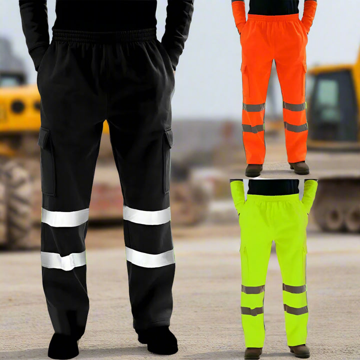 Three pairs of high-visibility reflective safety work pants in black, neon yellow, and safety orange displayed in front of a blurred construction site background with heavy machinery.