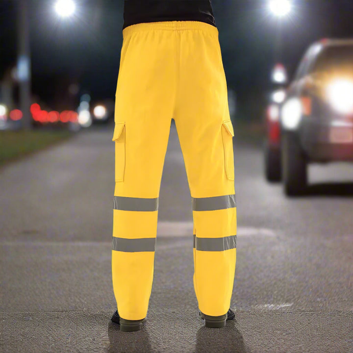 Bright yellow reflective safety pants showcased on a road at night with car headlights illuminating the background, emphasizing nighttime visibility.