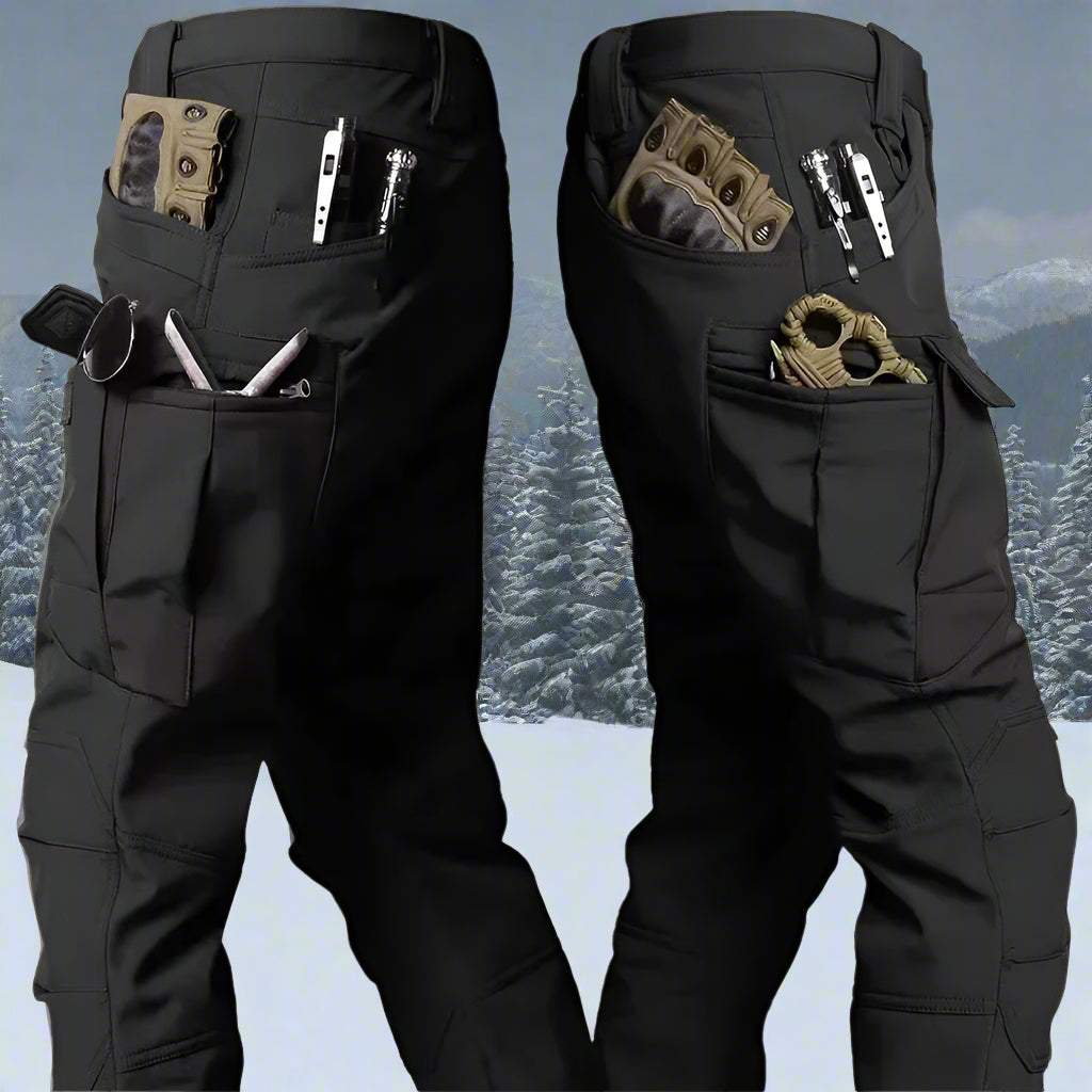 A military-style tactical winter jacket and pants set, designed with multiple pockets, a hood, and sharkskin fabric, displayed against a rugged snow-covered mountain backdrop. Built for durability, warmth, and mobility in harsh winter conditions.