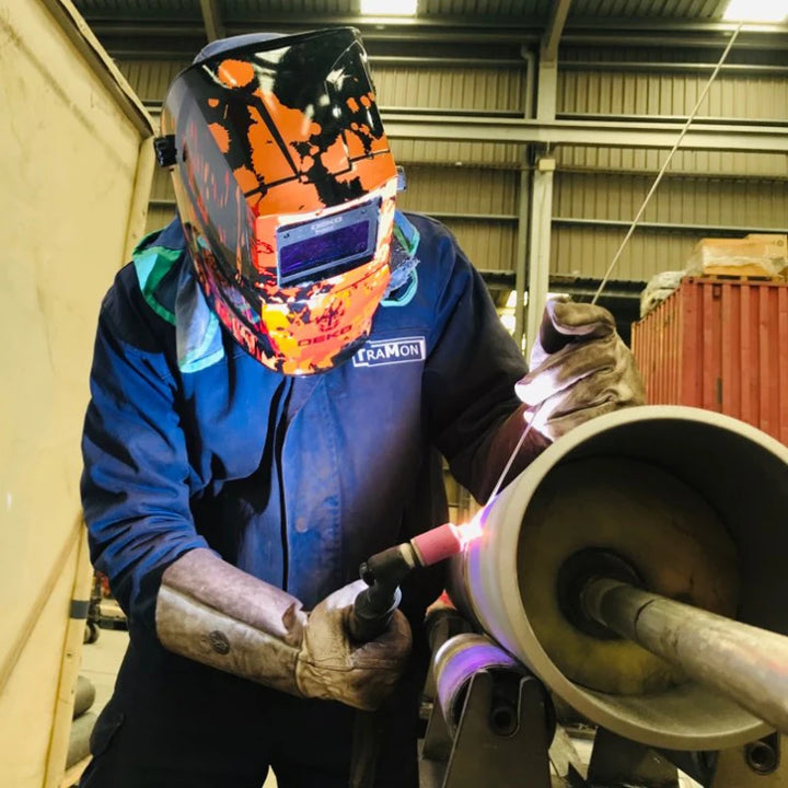 A professional welder using the DEKO welding helmet in an industrial setting with sparks flying.